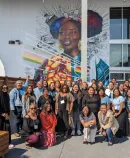 community leaders and advocates in front of a mural, gathered for connection, learning, and healing