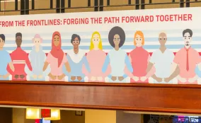Illustrated mural of diverse people standing shoulder to shoulder beneath text reading “From the frontlines: forging the path forward together”