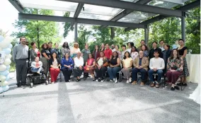 Group of staff members posing together at an outdoor gathering beneath a covered pavilion surrounded by trees.