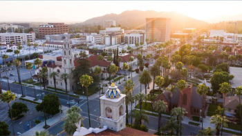 Aerial view of downtown San Jose at sunrise, with historic buildings, palm trees, and mountains in the background.