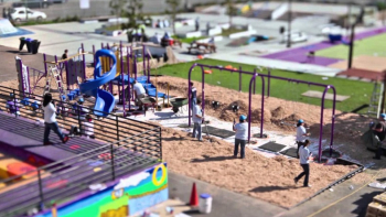 An aerial view of people using a colorful public plaza with seating, play features, and open space.