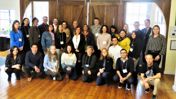 Group photo of conference attendees posing indoors on wood floors in front of large rustic sliding barn doors.
