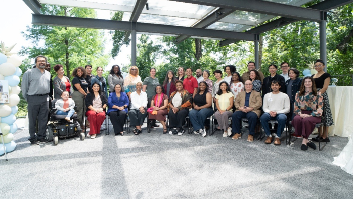 Group of staff members posing together at an outdoor gathering beneath a covered pavilion surrounded by trees.