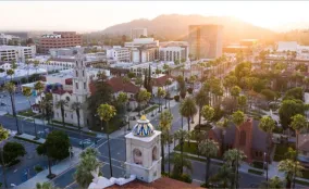 Aerial view of downtown San Jose at sunrise, with historic buildings, palm trees, and mountains in the background.